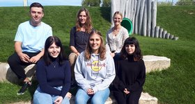 Foto: Glücklich mit dem FSJ; hintere Reihe von links: Nils Eckstein (FSJ); Heather Attwood, Regionalleitung Mannheim; Michelle Lerch, Kita-Leitung; vordere Reihe: Laura Wendler, Samira Klenk, Sarah Müller, alle FSJ 5 junge Frauen und 1 junger Mann sitzen auf einer Wiese