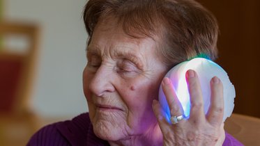 Seniorin hält sich den ichó Therapieball ans Ohr