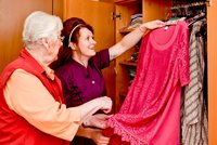 Eine Seniorin und eine Betreuungskraft wählen ein Kleid aus