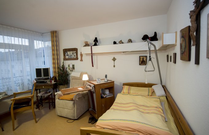 Bewohnerzimmer mit Pflegebett, Sessel und persönlichen Dekorationsgegenständen