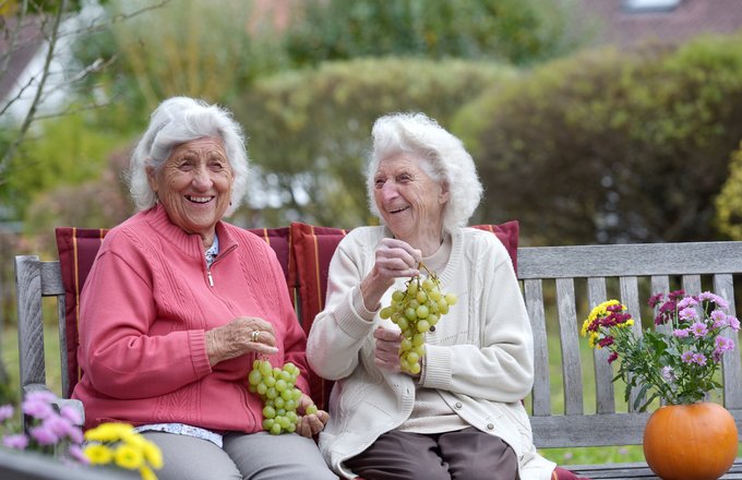 Zwei Seniorinnen mit Weintrauben sitzen draußen.