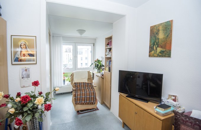 Möbiliertes Zimmer mit Sessel, TV und Blumenstrauß