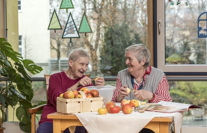 Zwei lachende Seniorinnen schälen gemeinsam Äpfel