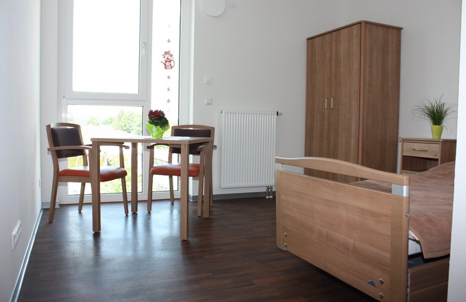 Pflegezimmer mit Tisch, zwei Stühlen, Schrank und Bett