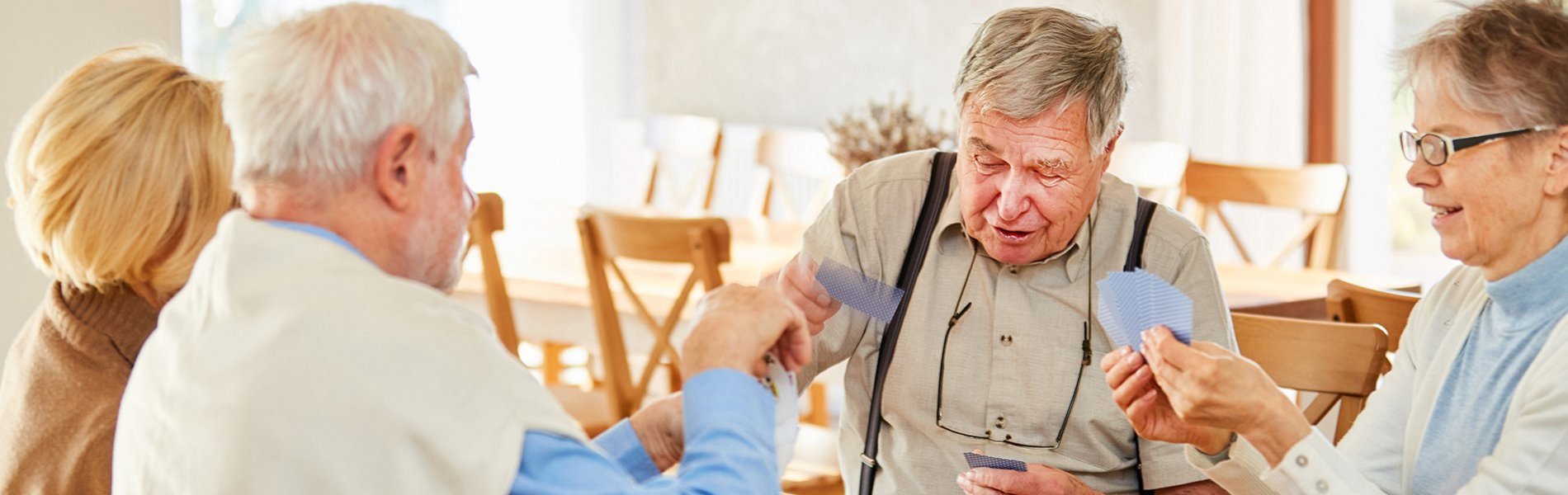 Vier Seniorinnen und Senioren sitzen gemeinsam am Tisch und spielen Karten.