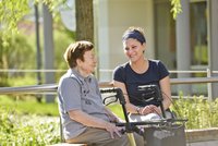 Seniorin und Betreuungskraft sitzen vor dem Haus an der Sonne