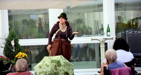 WPF 2021-07-Figurentheater Kumulus Frau mit Jägerhut und brauner Clownshose performt vor Publikum
