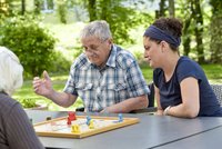 Senioren und Betreuungskraft spielen draußen ein Brettspiel