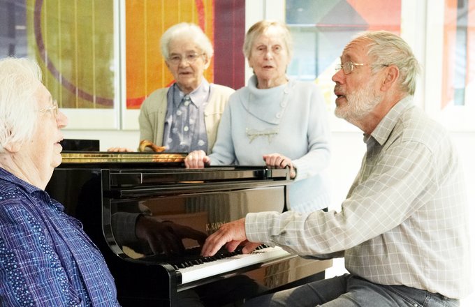 Ein Mann am Flügel begleitet singende Seniorinnen.