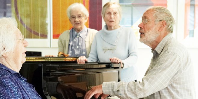 Ein Mann am Flügel begleitet singende Seniorinnen.